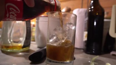 Bir adam gecenin 4 'ünde mutfakta buzlu rom bardağına siyah soda dolduruyor.