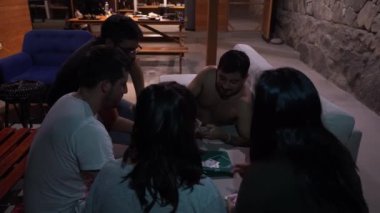 Birkaç arkadaş kadeh kaldırıyor ve kağıt oynuyor. Oyun salonda gergindi.