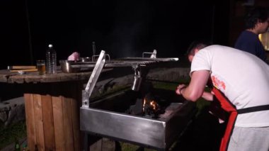 Bir adam gecenin 4 'ünde dağlık arazide bir kır evinde mangal için odun kömürü yakıyor.