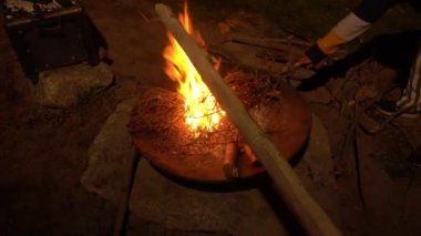 Gece 4k 'de bir kayanın üzerinde tahta dallar ve bambuyla kamp ateşini izleyip işaret ediyor.