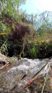 Güneşli bir günde, 4 km yükseklikteki dağlarda küçük bir şelale ile bir derenin dikey çekimi.