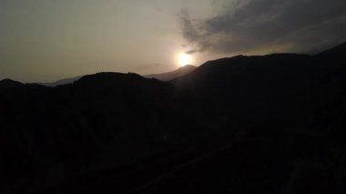 Hava aracının görüntüsü karanlık dağların arasından uzaklaşıyor. Güneş, günbatımında Lunahuana 'nın dağlık bölgelerinde parlıyor. Açık gökyüzü 4K' da.