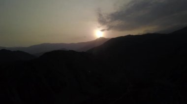 Hava aracının görüntüsü karanlık dağların arasından uzaklaşıyor. Güneş, günbatımında Lunahuana 'nın dağlık bölgelerinde parlıyor. Açık gökyüzü 4K' da.