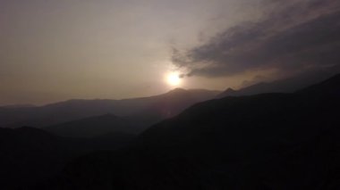 Karanlık dağlar arasındaki hava aracı görüntüsü. Arka planda güneş, günbatımında Lunahuana 'nın dağlık kesimlerinde parlıyor. Açık gökyüzü 4K.