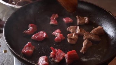 Yavaş çekimde tavada küçük kırmızı et parçaları pişirirken, elleri yağ sıçratan ve gündüzleri duman çıkaran ahşap bir sapı vardı.