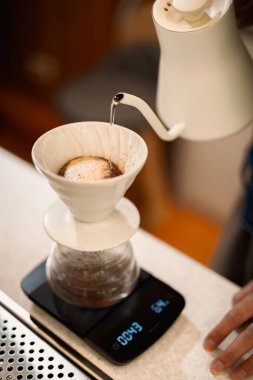 Barista damlatan bir kahve yapıyor. Kahve tozunun üzerine sıcak su döküyor.