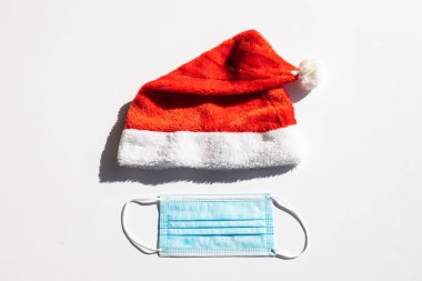 Noel Baba şapkası ve yüz maskesi beyazlar içinde izole edilmiş. Covid-19 konsepti.