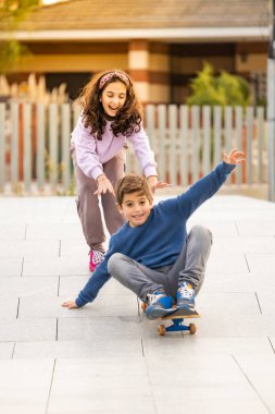 Two friends playing with a skate board clipart