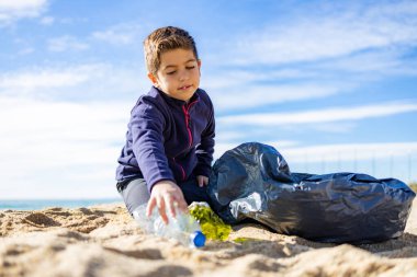 Plajda plastik toplayan küçük bir çocuk. Geri dönüşüm kavramı