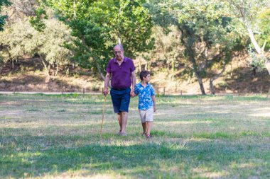 Küçük çocuk ve yaşlı adam tarlada yürüyor.