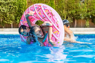Üç çocuk havuzda lastik bir yüzükle oynuyor.