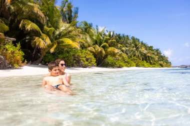 Anne ve oğlu Maldivler 'de bir plajda suda.