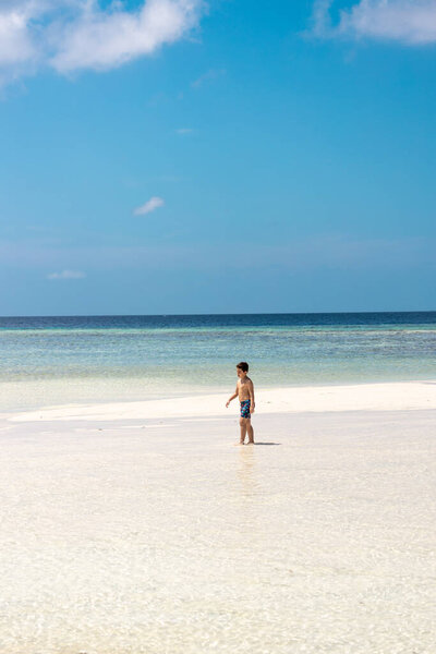 Little boy walking alone on a beach of turquoise water