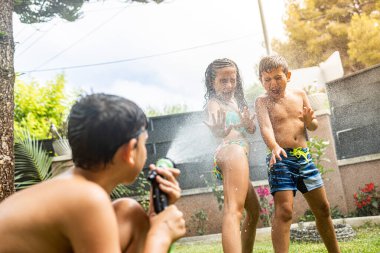 Bahçede hortumla oynayan üç komik çocuk.