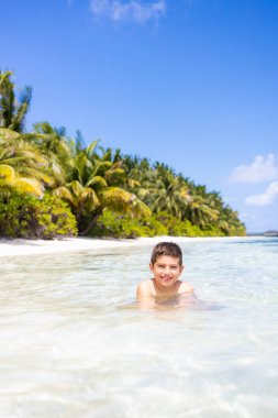 Tropik bir plajda suyun içinde küçük bir çocuk.