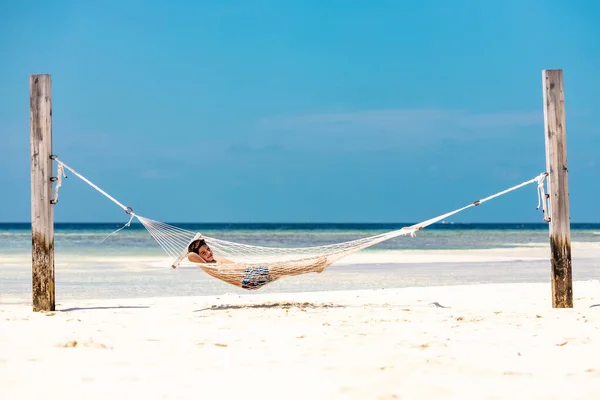 Little kid resting in a hammock on a white sand beach