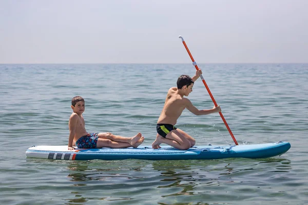 Two kids enyoying with a paddle surf in the sea on a summer day