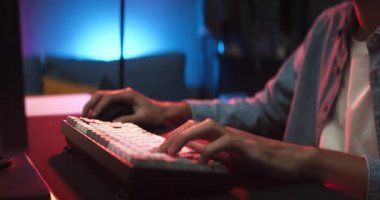 Genç Asyalı adam online bilgisayar oyunu oynuyor, renkli ışıklandırma yayını evde canlı yayında. Bir maçı kazanmanın coşkulu bir kutlaması. Oyuncu yaşam tarzı, E-Sport çevrimiçi oyun teknolojisi kavramı