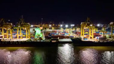 Bangkok, Thailand - Apr 25, 2022: Hyperlapse time-lapse of shipping port with cargo container ship, crane, in Asia city at night. Logistic industry or freight transportation concept, drone aerial view