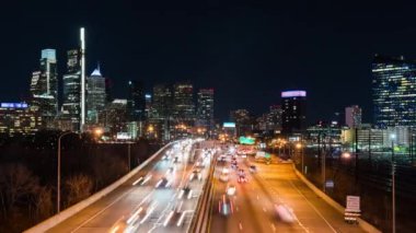 Time-lapse of car traffic transport on multiple lanes highway road, financial district buildings at night in Philadelphia, USA. America transportation, commuter lifestyle, American city life concept