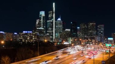 Time-lapse of car traffic transport on multiple lanes highway road, financial district buildings at night in Philadelphia, USA. America transportation, commuter lifestyle, American city life concept