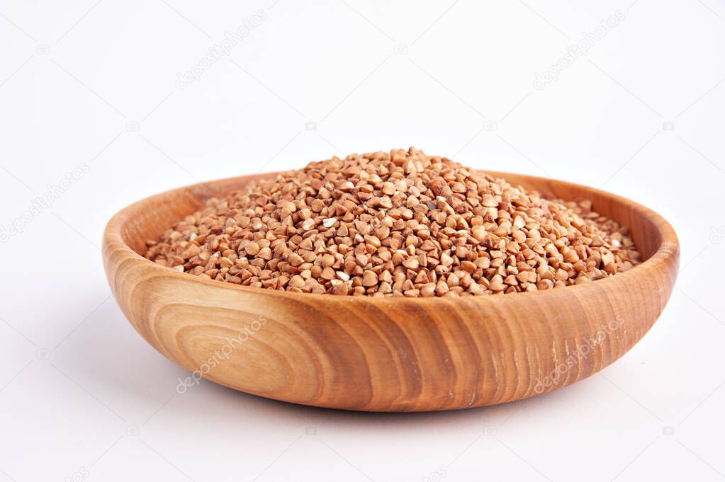 Raw buckwheat groats in a wooden bowl on a white background