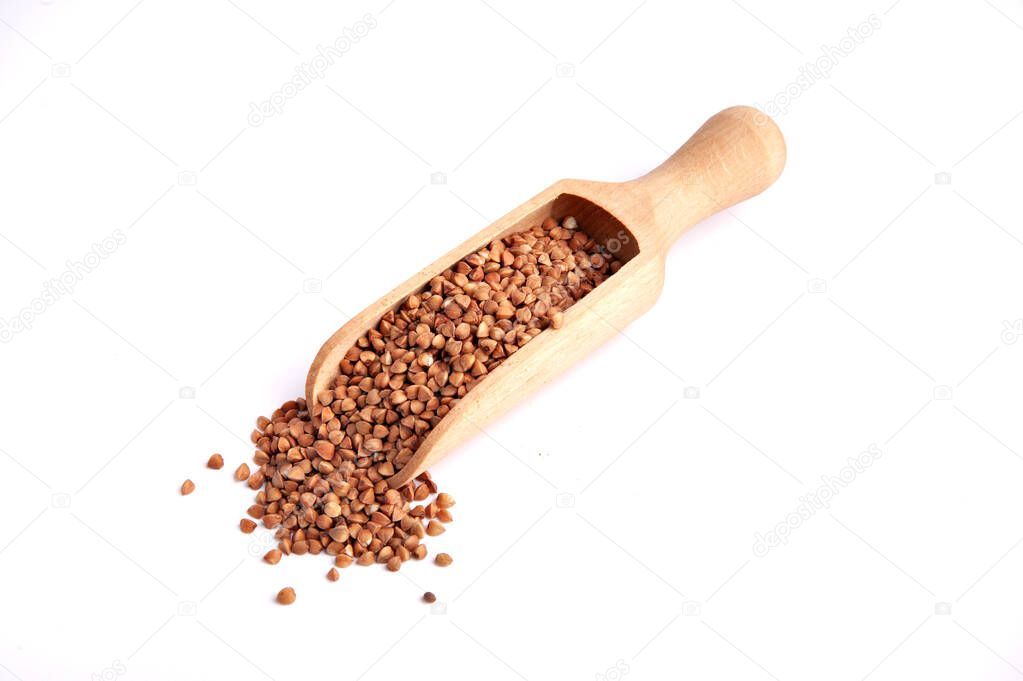 Buckwheat groats in a wooden scoop with groats nearby on a white background