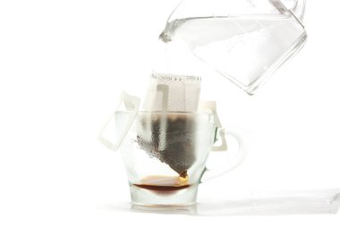 Amerikan kahvesini izole edilmiş beyaz arka plan damlaları yapmak için bardakla servis edilen sıcak suyu poşet kâğıt filtreye koyuyoruz.