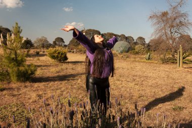 Meksikalı beyaz bir kadının bedeni baharda Meksika 'da çamlı, çiçekli ve kedili bir bahçede mor lavanta tarlaları arasında özgürce dönüyor.