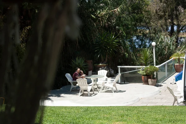 Caucasian man in home office job in the middle of the garden takes a call on his cell phone while typing on laptop messages works in professional occupation with digital nomadic freedom