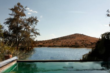 Scape ve Hill, gün batımında ağaçların ve bitkilerin arasında sonsuz havuzun yanında.