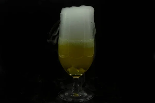 Beer glass containing fresh liquid with cooling dry ice cooling emanates white smoke outlining the profile of the glass in celebration of Halloween party