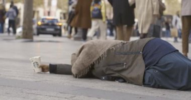 Paris 'te yayalar geçerken kaldırımda uzanmış dilenen bir kadın.