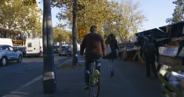 Paris street scene seniors on bikes along book-sellers — Vídeo de Stock