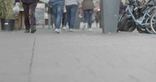 Slow motion pan of pedestrian feet on busy sidewalk ground level selective focus pan to gray wall — Stock Video