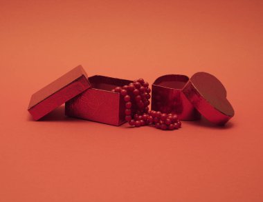 Kırmızı arka planda kırmızı inci kolyeli hediye kutuları. Noel ve Yeni Yıl geçmişi. Asgari tatil kavramı.