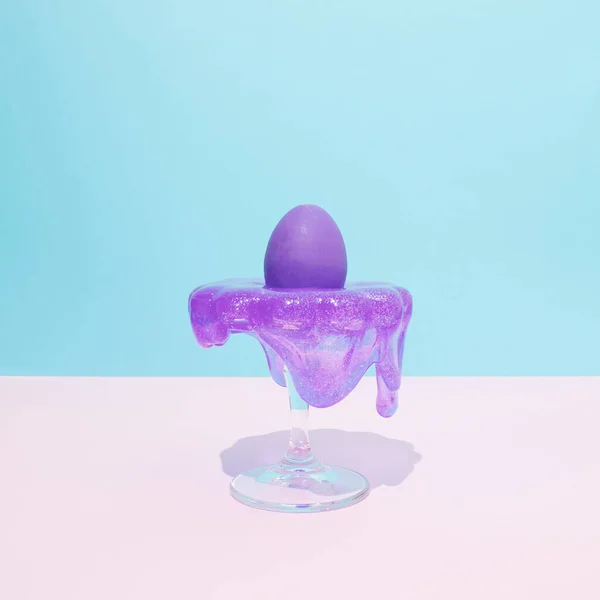 Cake holder with purple Easter egg and slime on pastel blue and white background. Creative food or Easter concept.