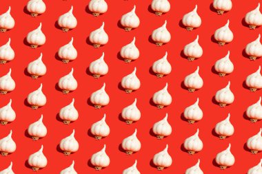 Kırmızı arka planda sarımsak desenli, renksiz bir desen. Yaratıcı bir sıcak, sağlıklı ya da aromatik gıda konsepti. İzometrik görünüm.