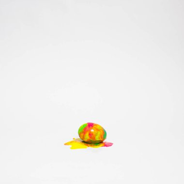 Paskalya yumurtası, beyaz arka planda boya damlıyor. Yumurtanın üzerine mavi, sarı, yeşil ve pembe renk döküldü. Yaratıcı tatil düzeni. En az çiğ gıda konsepti.