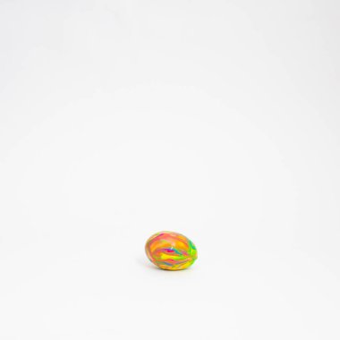 Paskalya yumurtası, beyaz arka planda boya damlıyor. Yumurtanın üzerine mavi, sarı, yeşil ve pembe renk döküldü. Yaratıcı tatil düzeni. En az çiğ gıda konsepti.