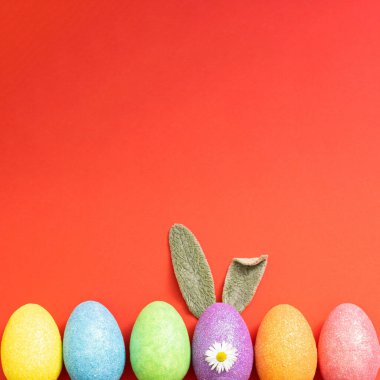 Kırmızı arka planda renkli Paskalya yumurtaları ve tavşan kulakları. Minimum tatil konsepti. Kopyalama alanı olan düz.