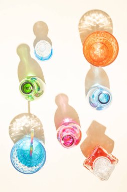 Kumlu arka planda soğuk içecekler olan renkli şişeler. Parlak renkli yansımalı gölgeler. Soyut estetik tasarım fikri. Güneşli plaj günü konsepti.