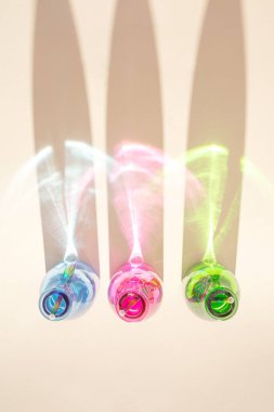 Kumlu arka planda soğuk içecekler olan renkli şişeler. Parlak renkli yansımalı gölgeler. Soyut estetik tasarım fikri. Güneşli plaj günü konsepti.