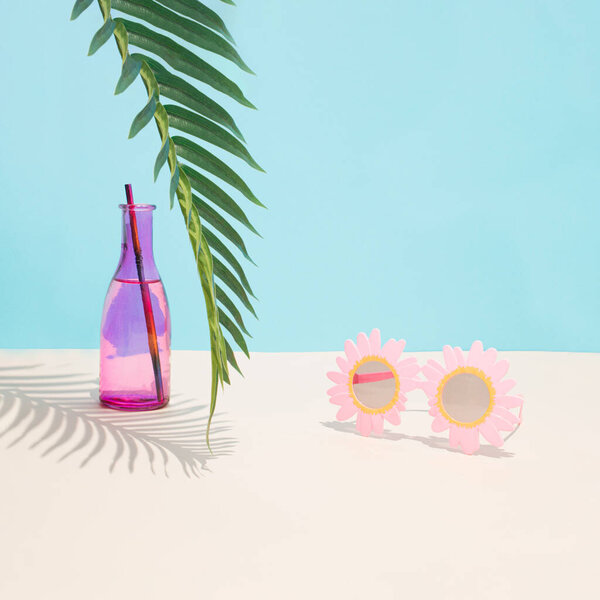 Cold pink drink in glass and funny sunglasses under green palm branch. Palm tree shadow imitating beach summer day. Aesthetic abstract design idea. Sunny beach day concept.