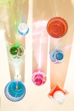 Kumlu arka planda soğuk içecekler olan renkli şişeler. Parlak renkli yansımalı gölgeler. Soyut estetik tasarım fikri. Güneşli plaj günü konsepti.