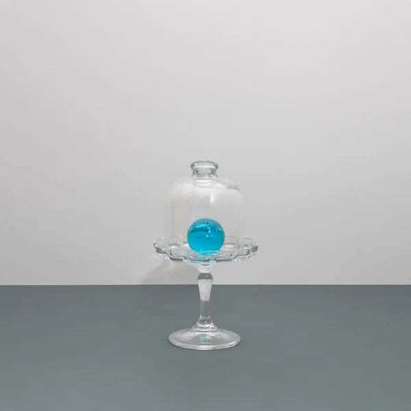 Glass blue ball in a cake holder against gray background. Abstract photo with glass, contrast and reflection.