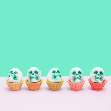 Five skulls in tart shells on turquoise and white. Halloween background.