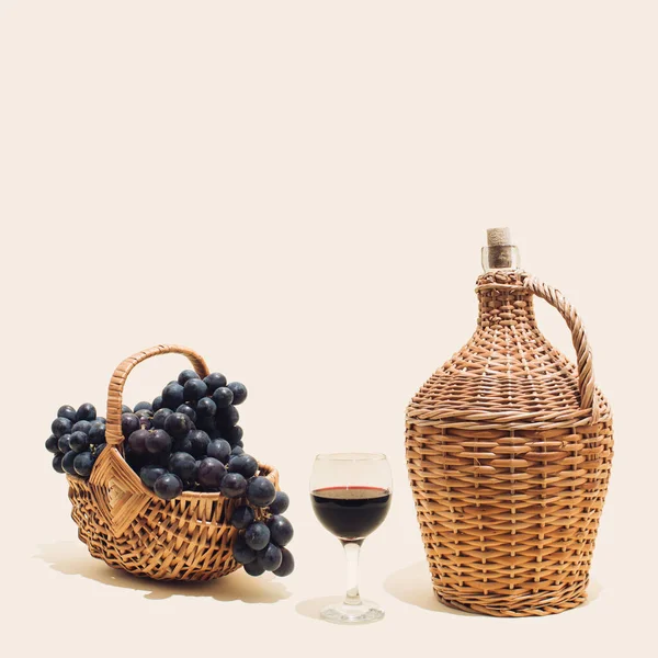 Aesthetic composition of blue grapes, glass of red wine and wicker basket full of fresh red grapes. Autumn harvest, vineyard concept.