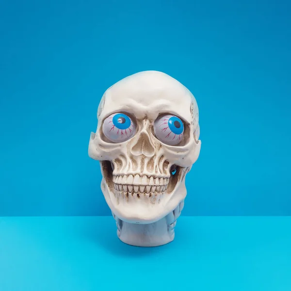 Realistic human skull with bright blue eyes making silly face. Funny spooky Halloween composition.