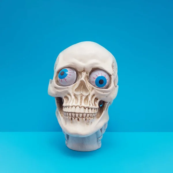 Realistic human skull with bright blue eyes making silly face. Funny spooky Halloween composition.